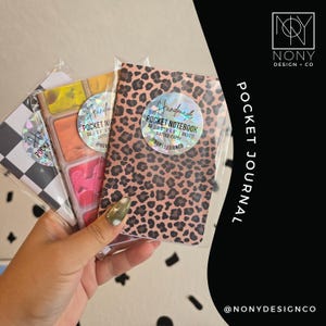 May include: Three A6 pocket notebooks measuring 3.5 inches by 5.5 inches with dotted paper. One features a brown and black leopard print, another a multi-colored paint palette design, and the third a black and white checkered pattern.