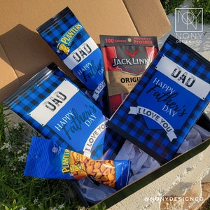 Op de afbeelding: Een cadeaupakket voor Vaderdag met snacks. Het bevat blauw geruite zakken met de tekst "DAD Happy Father's Day I Love You", een verpakking Jack Link's beef jerky en Planters pinda's.