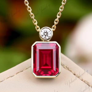 May include: A gold chain necklace with a pendant featuring a large, square-shaped, red gemstone and a smaller, round, clear gemstone.