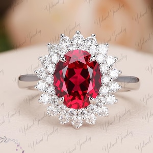 Op de afbeelding: Een zilveren ring met een grote ovale robijn, omringd door een halo van kleinere diamanten.