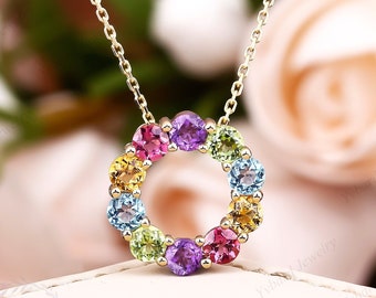 May include: A gold chain necklace with a pendant featuring a circle of colorful gemstones. The gemstones are arranged in a rainbow pattern, with red, orange, yellow, green, blue, and purple stones.