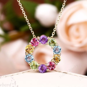 May include: A gold chain necklace with a pendant featuring a circle of colorful gemstones. The gemstones are arranged in a rainbow pattern, with red, orange, yellow, green, blue, and purple stones.