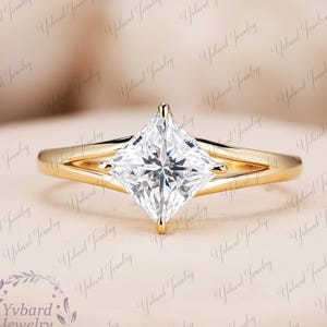 Op de afbeelding: Een gouden verlovingsring met een princess-geslepen diamant. De ring heeft een split-schacht ontwerp, waarbij de band aan weerszijden van de diamant splitst. De diamant is gezet in een vier-klauwzetting.