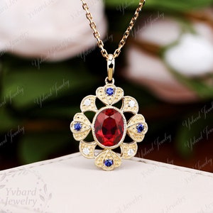May include: A gold pendant necklace featuring a red oval gemstone set within a delicate floral design with blue and white accents.