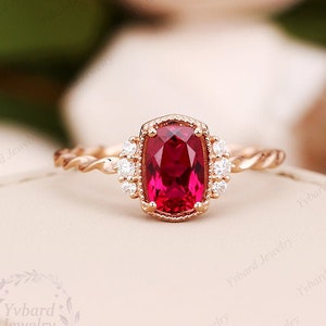 May include: A rose gold engagement ring with a large, cushion-cut ruby gemstone surrounded by smaller diamonds. The band is twisted and features a delicate, detailed design.
