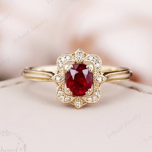 Op de afbeelding: Een gouden ring met een rode ovale edelsteen omringd door kleinere witte edelstenen in een delicate filigraan setting.