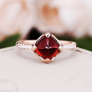 May include: A rose gold ring with a square red gemstone and a band of small clear gemstones.