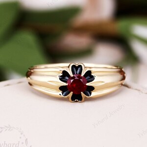 May include: A gold ring with a black enamel flower design and a red gemstone in the center.