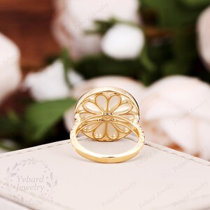 May include: A gold ring with a white flower-shaped stone set in a halo of smaller stones. The ring is on a white background.