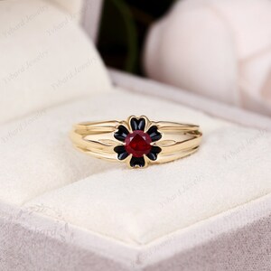 May include: A gold ring with a black flower design and a red gemstone in the center.