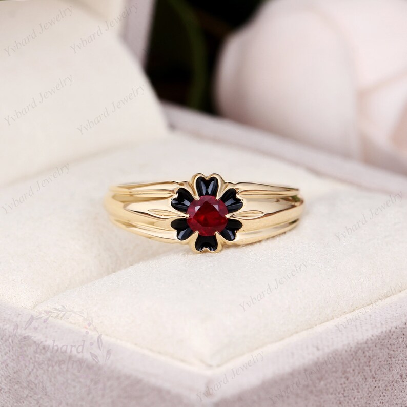 May include: A gold ring with a black flower design and a red gemstone in the center.