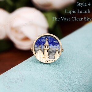May include: A gold ring with a lapis lazuli stone set in a round bezel. The stone features a detailed cityscape design with a tall tower and smaller buildings. The ring is on a blue background. "Style 4 Lapis Lazuli The Vast Clear Sky" is written in white text on a white background.