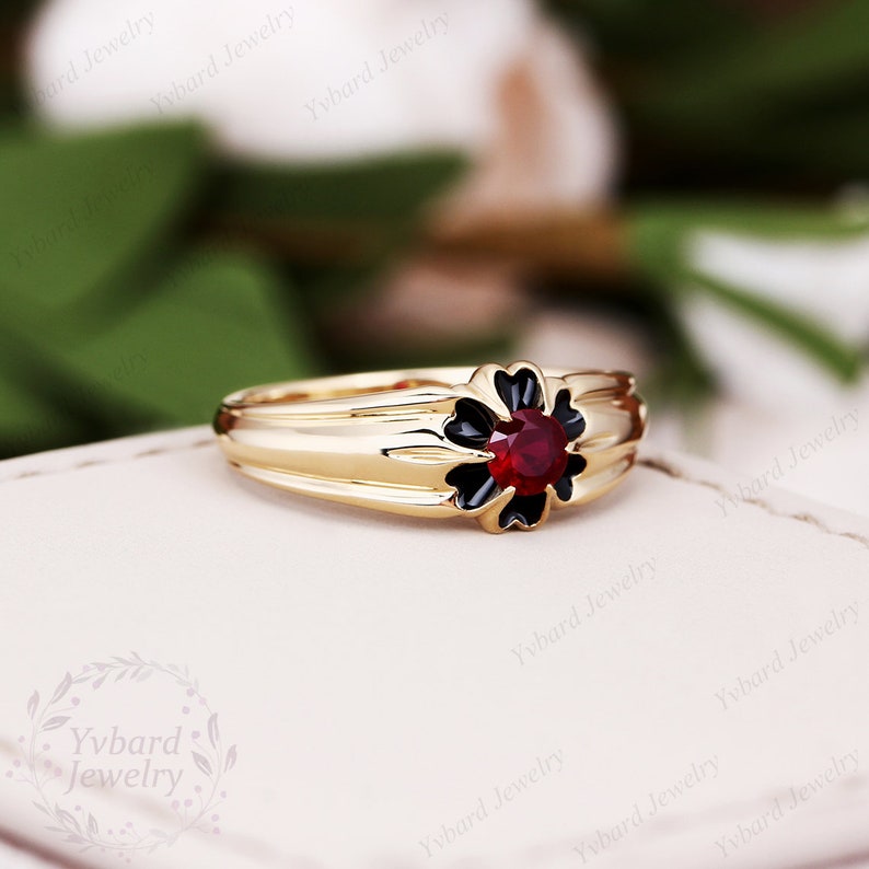 May include: A gold ring with a black flower design and a red gemstone in the center.