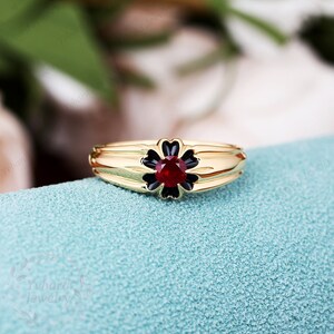 May include: A gold ring with a black flower design and a red gemstone in the center.