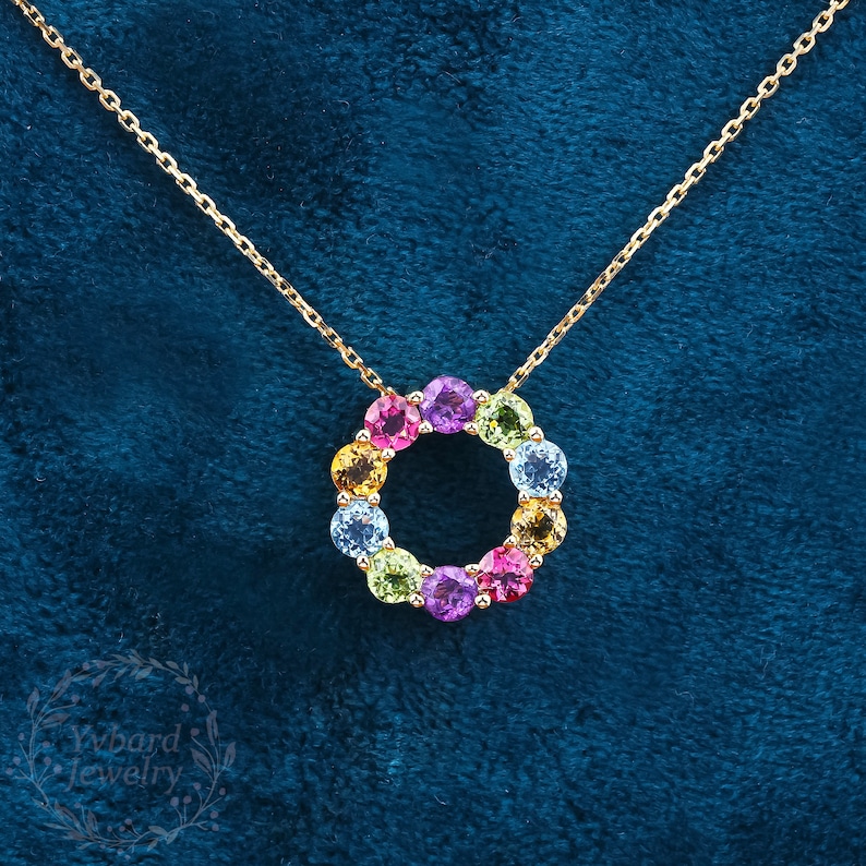 May include: A gold chain necklace with a pendant featuring a circle of colorful gemstones. The gemstones are arranged in a rainbow pattern, with red, orange, yellow, green, blue, and purple stones.