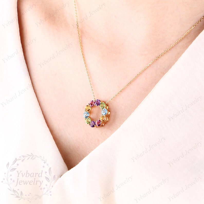 May include: A gold necklace with a circular pendant featuring a ring of colorful gemstones. The pendant is made of gold and features a variety of gemstones, including amethyst, citrine, peridot, aquamarine, and topaz.