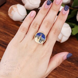 May include: Gold ring with a blue and white stone featuring a detailed cityscape design.