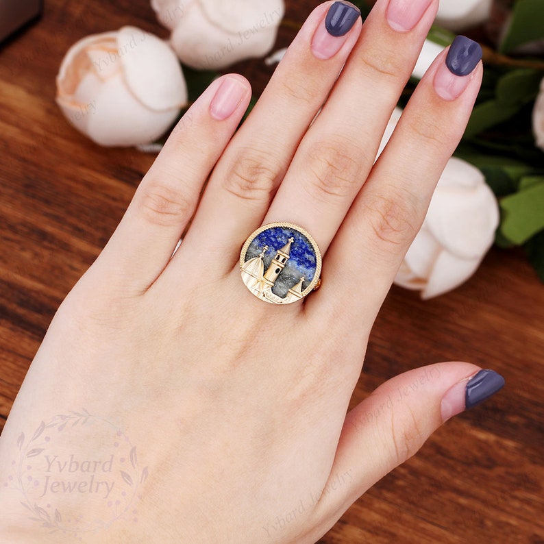 May include: Gold ring with a blue and white stone featuring a detailed cityscape design.