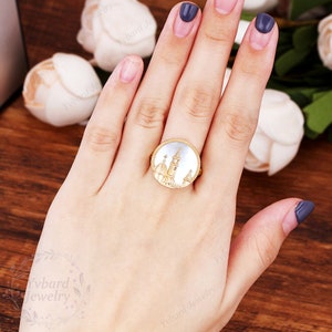 May include: A gold ring with a white cameo featuring a detailed design of a church building.