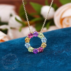 May include: A gold chain necklace with a pendant featuring a circle of colorful gemstones. The gemstones are arranged in a rainbow pattern, with red, orange, yellow, green, blue, and purple stones.
