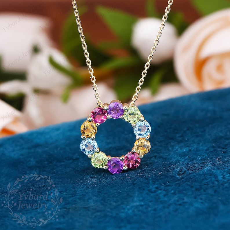 May include: A gold chain necklace with a pendant featuring a circle of colorful gemstones. The gemstones are arranged in a rainbow pattern, with red, orange, yellow, green, blue, and purple stones.