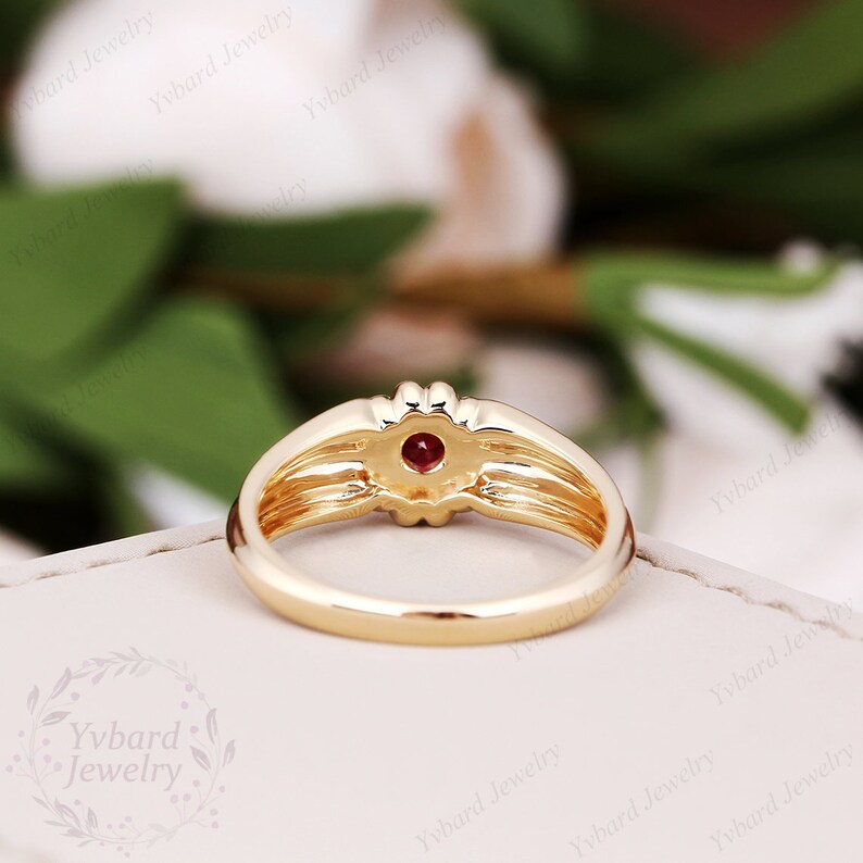 May include: A gold ring with a red gemstone set in the center. The ring has a textured band with multiple grooves.
