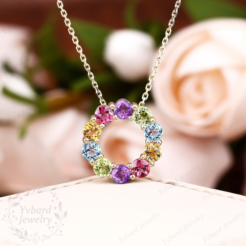 May include: A gold chain necklace with a pendant featuring a circle of colorful gemstones. The gemstones are arranged in a rainbow pattern, with red, orange, yellow, green, blue, and purple stones.