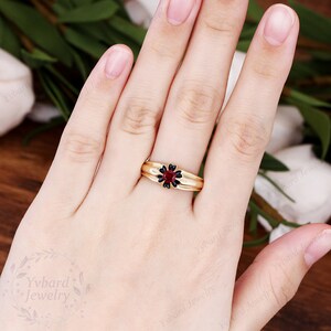 May include: A gold ring with a black flower design and a red gemstone in the center.