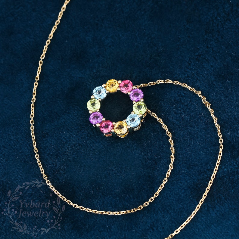 May include: A gold chain necklace with a pendant featuring a circle of colorful gemstones. The pendant is made of gold and has a variety of gemstones in different colors, including pink, yellow, blue, green, and orange.