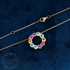 May include: A gold chain necklace with a pendant featuring a circle of colorful gemstones. The gemstones are arranged in a rainbow pattern, with red, orange, yellow, green, blue, and purple stones.