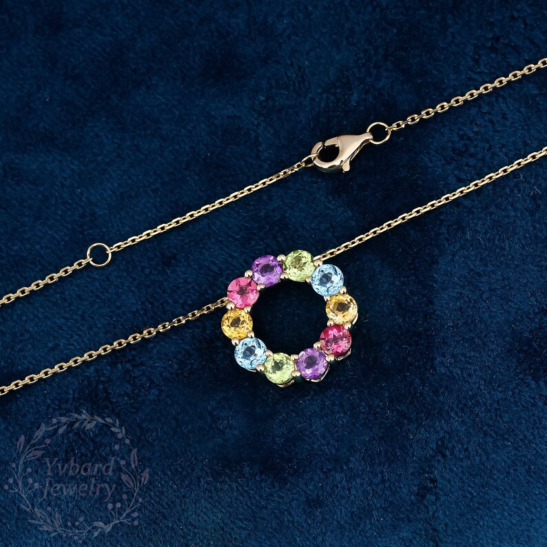 May include: A gold chain necklace with a pendant featuring a circle of colorful gemstones. The gemstones are arranged in a rainbow pattern, with red, orange, yellow, green, blue, and purple stones.
