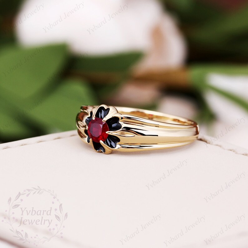 May include: A gold ring with a black enamel flower design and a red gemstone in the center.