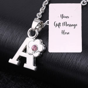May include: Silver necklace featuring a letter A charm and a pink flower with a rhinestone. The necklace includes a blank card that reads "Your Gift Message Here".