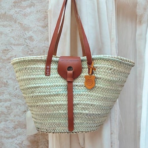 May include: A white woven tote bag with brown leather handles and a brown leather strap. The bag has a tag that says "Art-Of-Handmade".