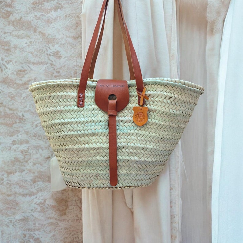 May include: A white woven tote bag with brown leather handles and a brown leather strap. The bag has a tag that says "Art-Of-Handmade".