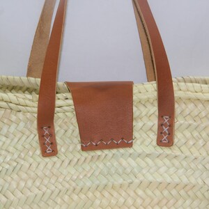 May include: A woven straw tote bag with brown leather handles and a brown leather patch on the front.