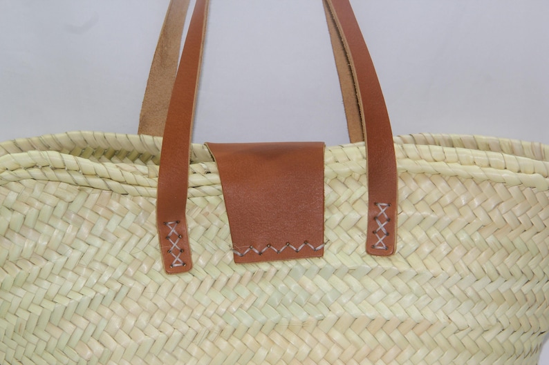 May include: A woven straw tote bag with brown leather handles and a brown leather patch on the front.