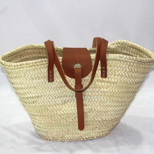 May include: A large, woven straw tote bag with brown leather handles and a flap closure. The bag has a natural, light beige color and a herringbone weave pattern.