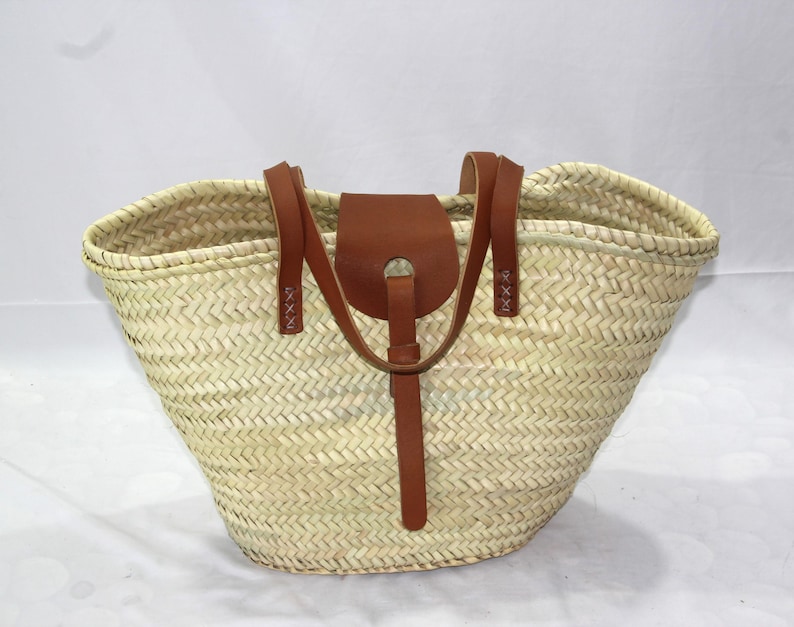 May include: A large, woven straw tote bag with brown leather handles and a flap closure. The bag has a natural, light beige color and a herringbone weave pattern.