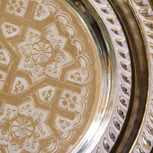 Peut inclure: Un ensemble de trois plateaux ronds en m&eacute;tal avec des motifs grav&eacute;s complexes. Les plateaux sont imbriqu&eacute;s, le plus grand en bas et le plus petit en haut. Les plateaux sont de couleur or brillant.