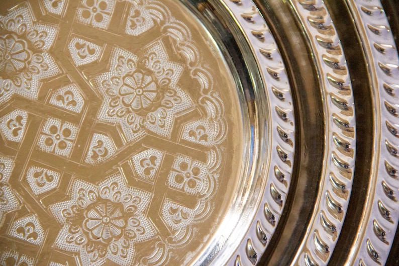 Peut inclure: Un ensemble de trois plateaux ronds en m&eacute;tal avec des motifs grav&eacute;s complexes. Les plateaux sont imbriqu&eacute;s, le plus grand en bas et le plus petit en haut. Les plateaux sont de couleur or brillant.