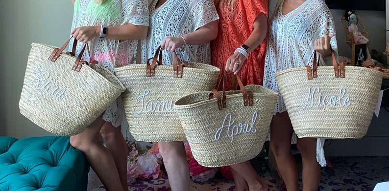 Puede incluir: Cuatro bolsas de mimbre con asas de cuero y nombres bordados en blanco:  "Rian", "Jamie", "April" y "Nicole".