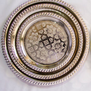 Peut inclure: Un ensemble de trois plateaux de service en argent plaqu&eacute; avec des motifs en relief complexes. Les plateaux sont imbriqu&eacute;s, le plus petit plateau pr&eacute;sentant un motif floral.