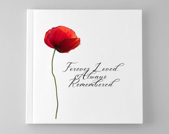 Puede incluir: Una cubierta de libro cuadrada de color blanco que presenta una sola amapola roja vibrante en el lado izquierdo. A la derecha de la flor, el texto negro en cursiva dice: Forever Loved. Always Remembered. El diseño es limpio y centrado.