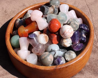 May include: A wooden bowl filled with a variety of polished gemstones in different shapes and colors. The gemstones include pink, red, purple, and green stones. The bowl is made of a light brown wood.