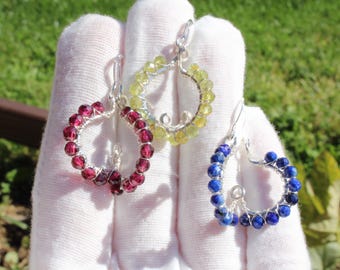 May include: Three pairs of heart-shaped earrings. One pair features red gemstones, another yellow, and the third blue. Each earring is crafted with a silver wire frame and a series of small, round gemstones. The earrings are displayed against a white background.