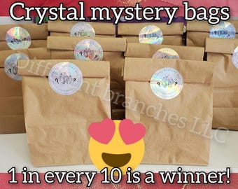 May include: A collection of brown paper bags labeled "Crystal mystery bags" with holographic stickers. The text "1 in every 10 is a winner!" is displayed below the bags. The bags are arranged on a white surface.