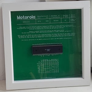 May include: A framed display of a Motorola 68000 microprocessor. The green background features technical details, manufacturing dates (1979-1996), and a diagram. The white frame surrounds the display. Text includes transistor count, bits, and clock speed.