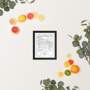 May include: A black-framed document with grey text, surrounded by fresh citrus fruits like lemons, grapefruits, and oranges, and green foliage. The arrangement creates a visually appealing contrast of the document's formality with the natural elements.