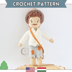 May include: Crochet pattern for a doll with brown hair, a white shirt, blue pants, and a brown hat. The doll is holding a brown strap. The pattern is available for purchase on Etsy.